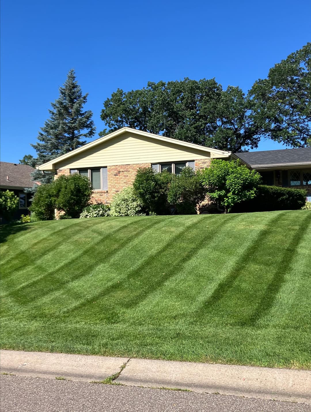 Well-maintained brick house with lush green lawn and trees under a clear blue sky.