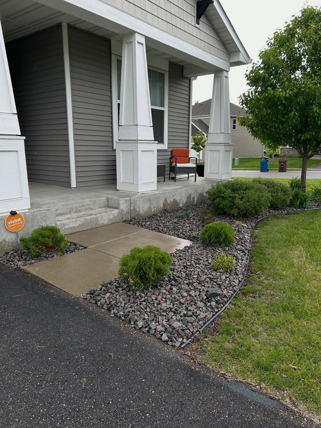 Residential porch with a chair, landscaped path, and ornamental shrubs.