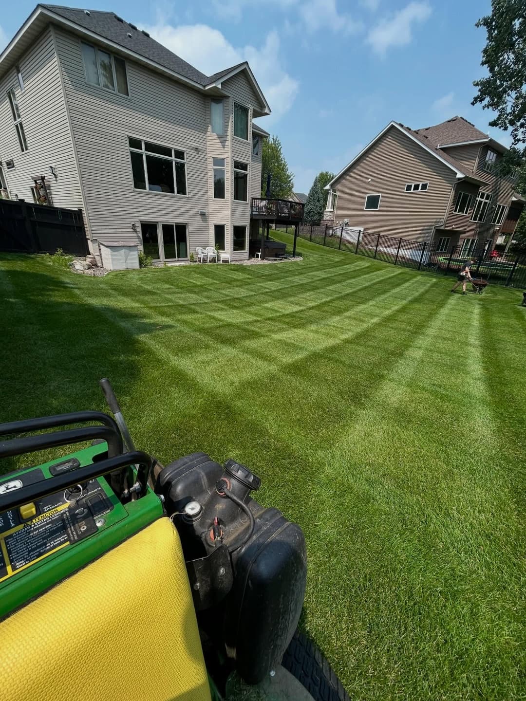 View of a neatly striped lawn with a riding mower in the foreground and houses in the background.