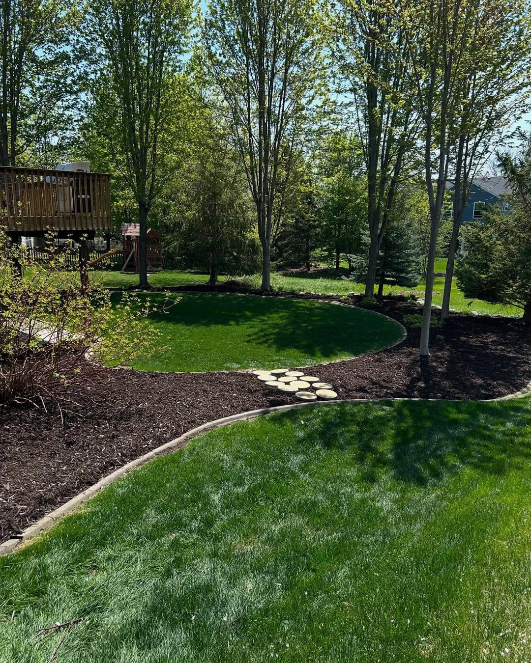 Lush green backyard with curved stone path and landscaped trees on a sunny day.